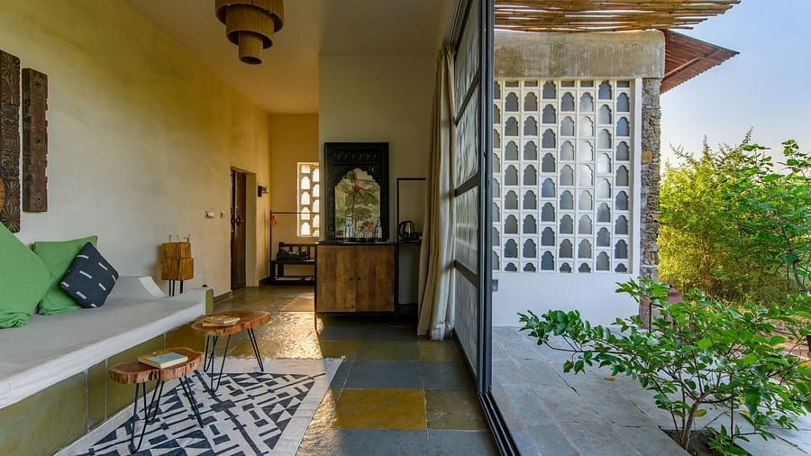 An image of a room with a queen size bed, chandelier, ceiling fan, other decorative items and an expansive glass door leading out - Utsav Camp Sariska