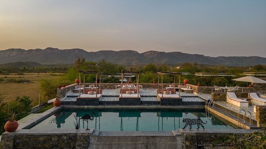 An image of a seating arrangement near the swimming pool in the open with the backdrop of sunset - Utsav Camp Sariska