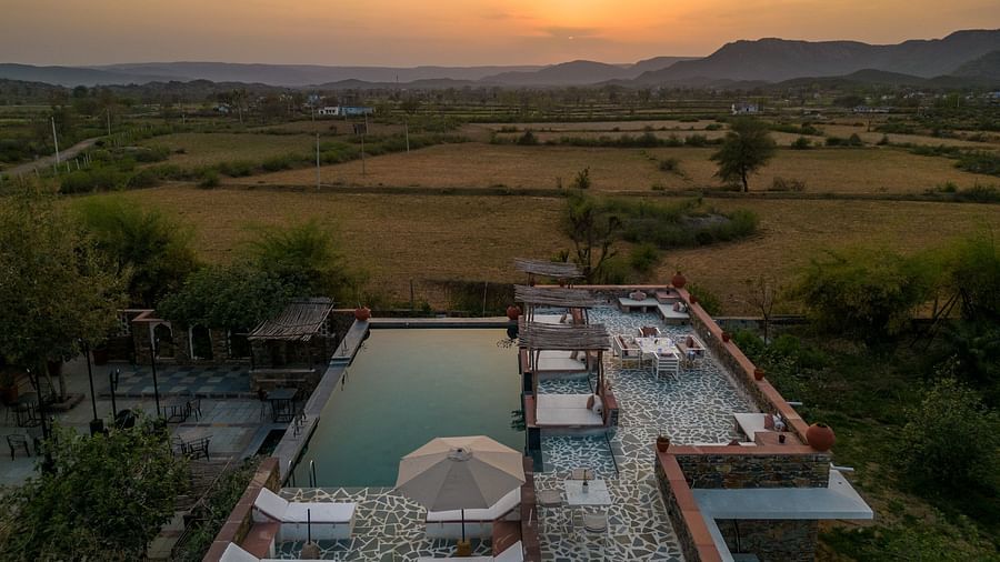 An image of a seating arrangement near the swimming pool in the open with the backdrop of sunset - Utsav Camp Sariska