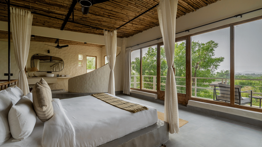 Bedroom with canopy bed, large windows, wooden ceiling, and serene outdoor views.