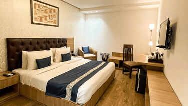 A wide-angle view of an executive room featuring a bed with a navy blue runner, hardwood floors, and minimalist modern decor - Hotel 91 HUDA City Centre, Gurugram
