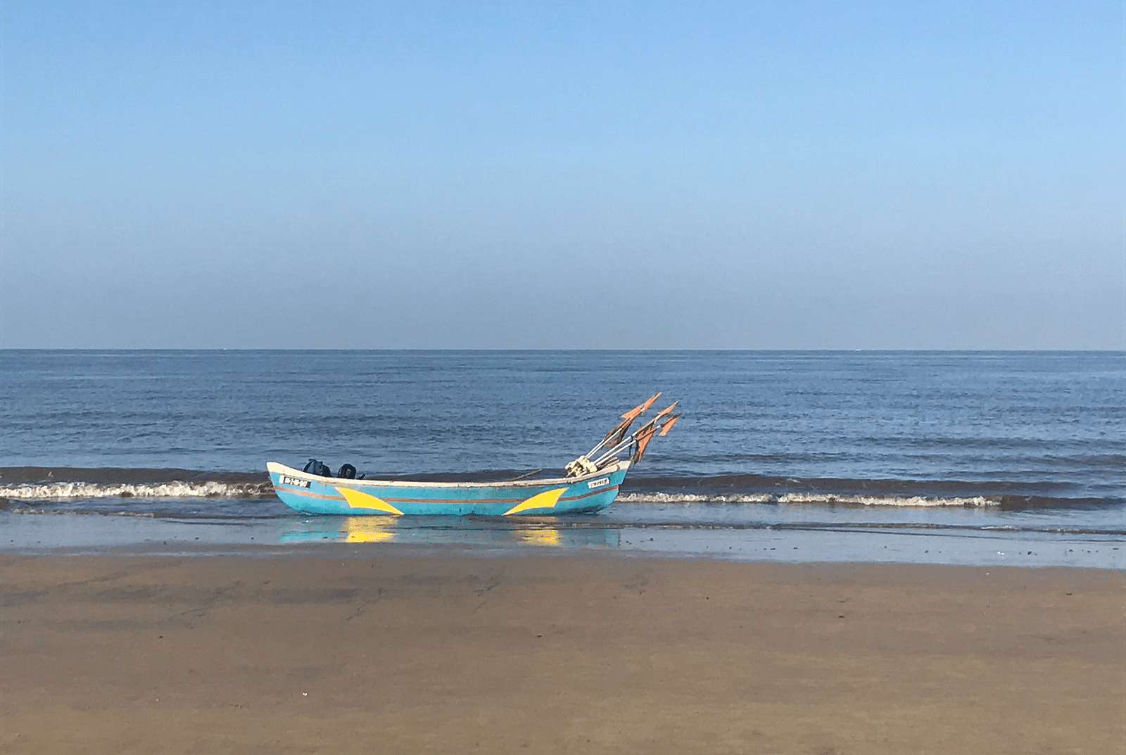 a solitary boat on the shores on Juhu beach with blue skies in the background.