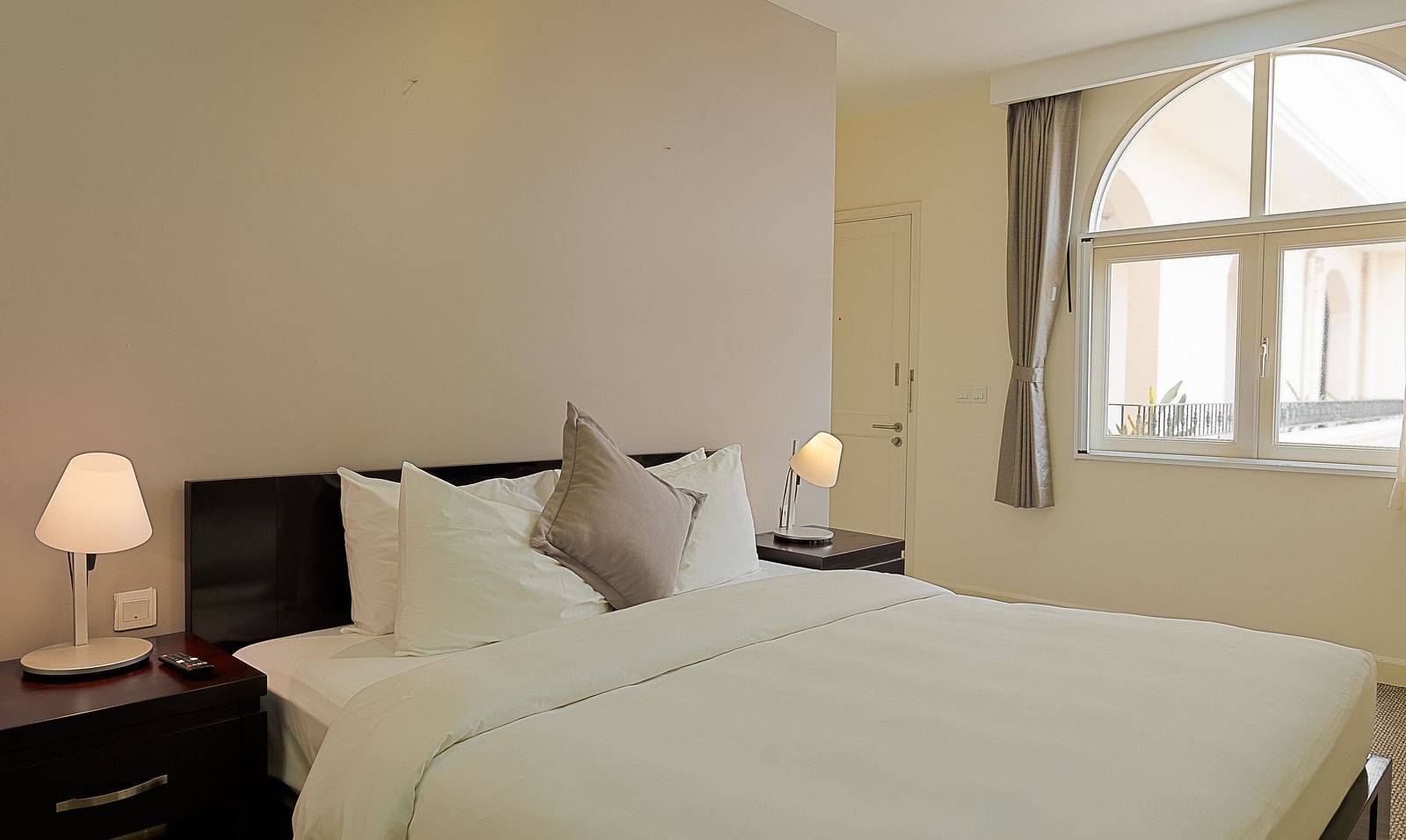A room with a white bed, bedside tables, lamps, and a large window | Four-bedroom Suite | Central Mansions, Phnom Penh
