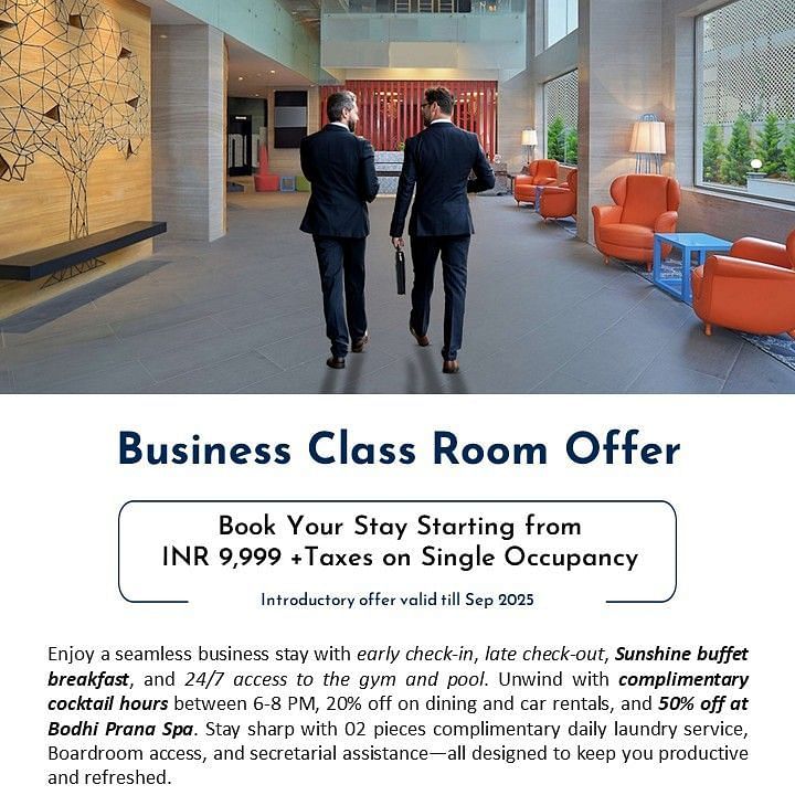 Creative corporate photography showing two businessmen in suits walking through the modern, spacious lobby of Radisson Bengaluru City Center Ulsoor Lake, featuring contemporary design elements and orange accent furniture, promoting the Business Class Room 