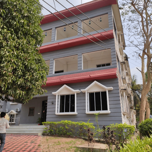 The facade of Lake Side Resort Neermahal, featuring trees surrounding the building.