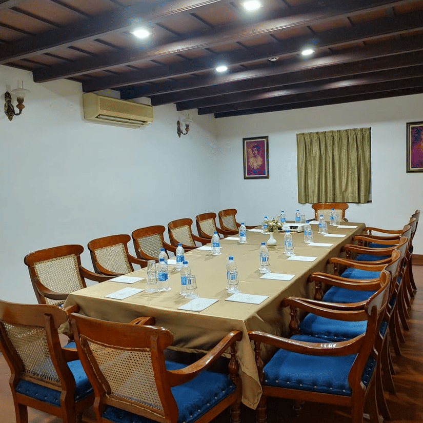 Boardroom with a long wooden table, blue-cushioned chairs, and a traditional wooden ceiling, offering one of the ideal meeting rooms in Trivandrum at The Travancore Heritage Beach Resort.