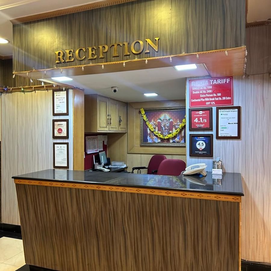 Reception area at Hotel Swagath, Bangalore with wooden front desk, wall decor, and bright lighting.