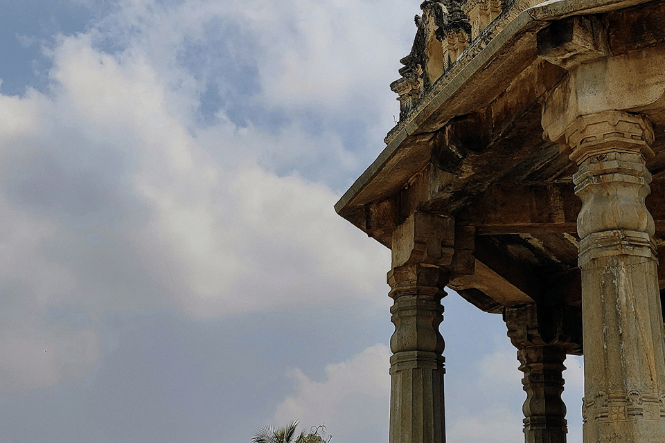 Carved stone pillared mantapa against a cloudy sky at Melkote