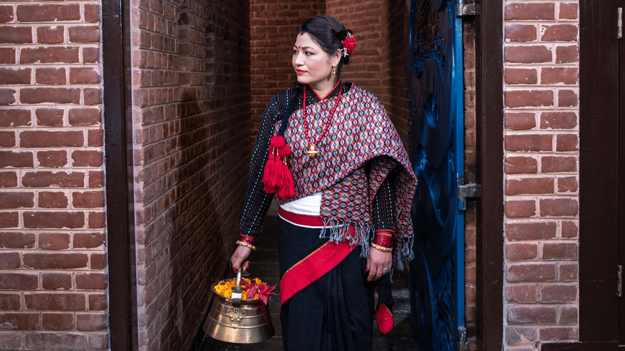 A woman in elegant attire walking through a traditional wooden doorway of a red brick heritage building in Bhaktapur, Nepal.