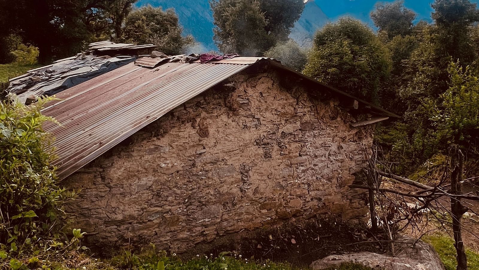 Image of a stone house in a village with scattered clouds in the sky | Faraway Cottages, Auli