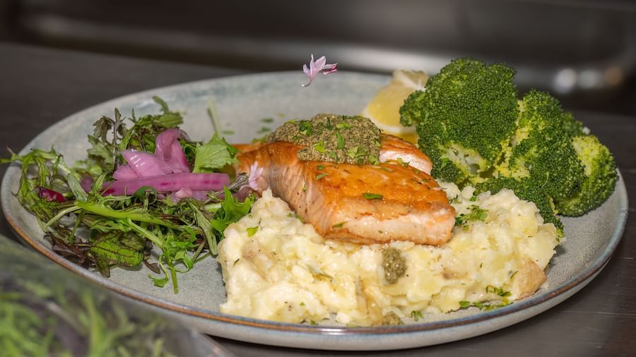 Close-up of salmon fillet being plated with mashed potatoes and broccoli in the kitchen at Narrow Gauge Inn.