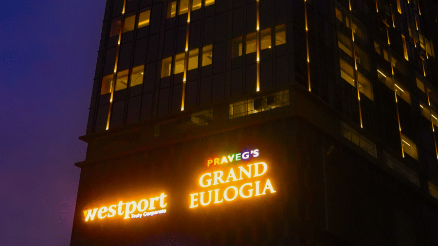 A vertical shot of the tall hotel building with glowing signage under a dark blue sky - Praveg's Grand Eulogia, Ahmedabad