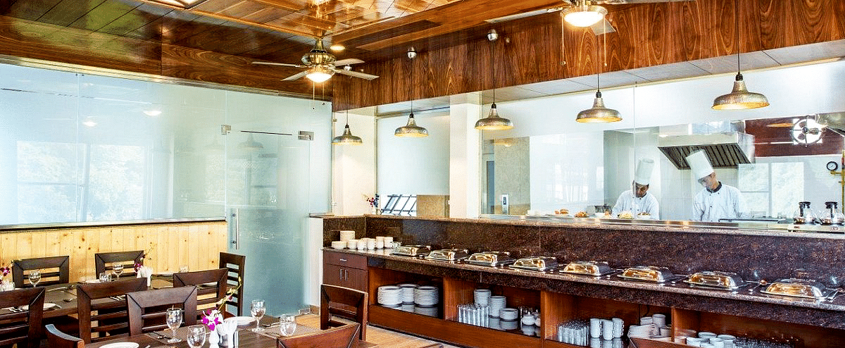 The restaurant at Regenta Inn DLS featuring the kitchen separated by a glass partition with a buffet counter in front of it.