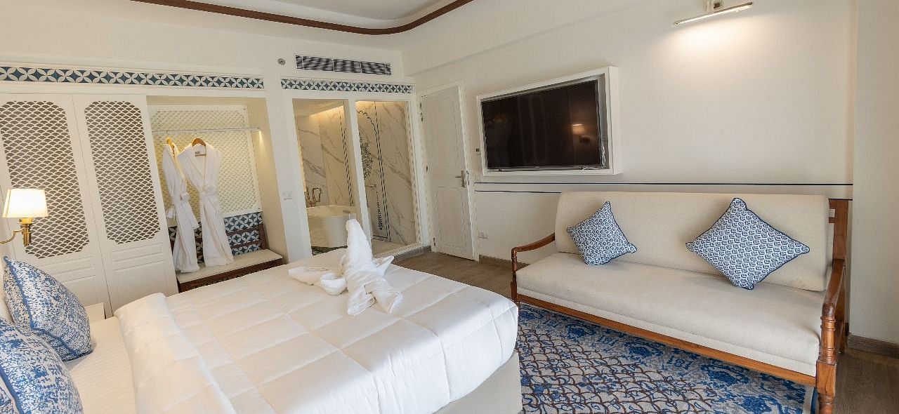 Corner view shot of the bedroom at Ananata Room featuring a plush double bed alon with a television and a couch in front of it at Bhagirathi by RDB Atishay.
