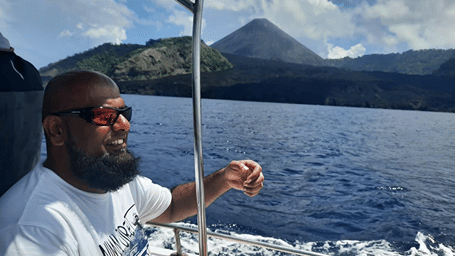 Guest in sunglasses and a white t-shirt on the boat looking across the sea at Barren Island volcano, on a trip by Matsya Island Retreat by Island Quest