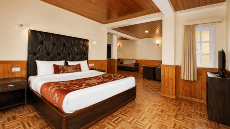 A bed sits in the centre of the Junior Suite at Orsino Khangri Karpo Retreat & Spa, Lachung. Wood panelling covers the walls and ceiling. A window and a television stand in the corner.