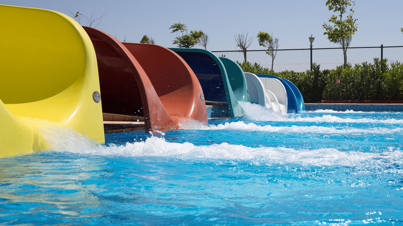 A row of multi-coloured water slides emptying into a bright blue swimming pool at a water park.