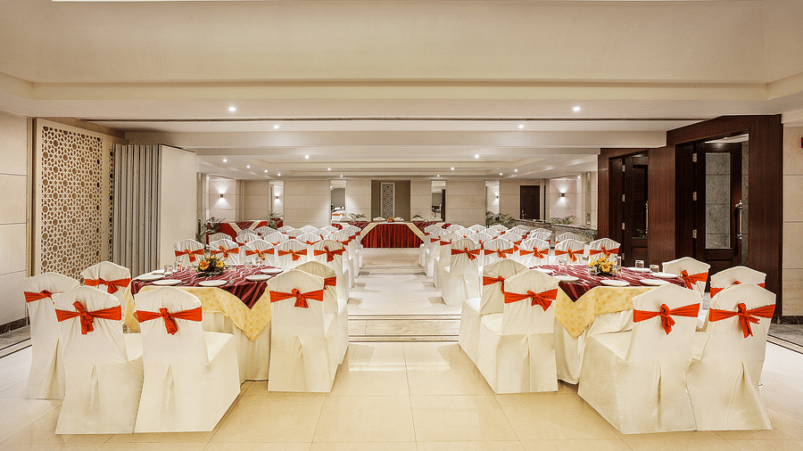 an image of an event space showing a well-spaced seating arrangement with white chairs tied with red bows - The Manor, Bareilly
