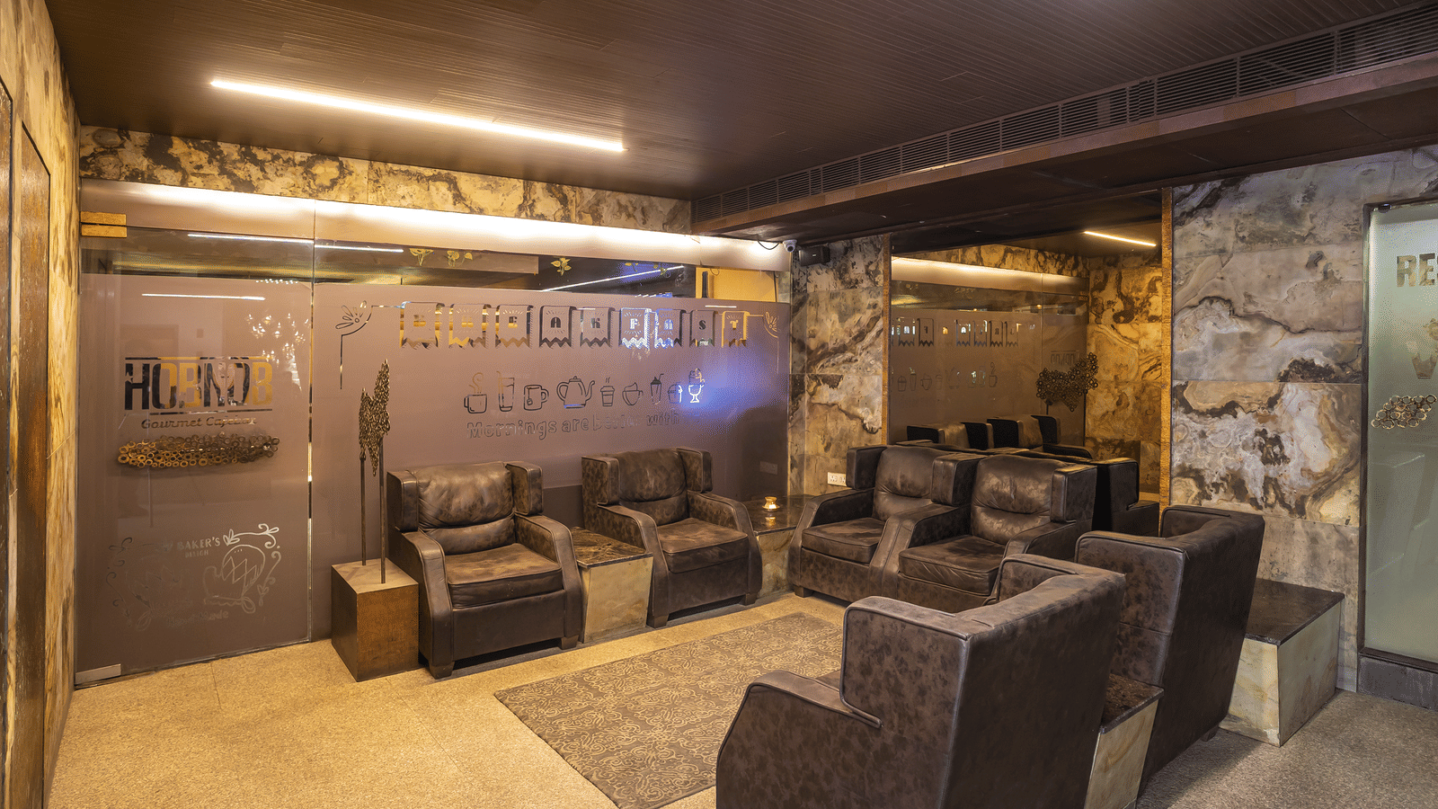 Indoor lounge area with brown cushioned seats, soft lighting, and walls decorated with travel-themed graphics at Infiniti Hotel, Indore.