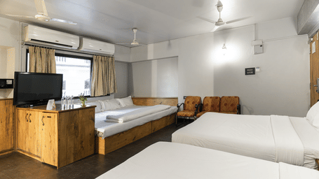 A room with multiple beds, wooden furniture and a television at Infiniti Hotel, Indore.