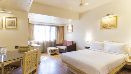 Bedroom with a king size bed, dining table & chairs, a seating space by the window and painting on the wall at Infiniti Hotel, Indore.