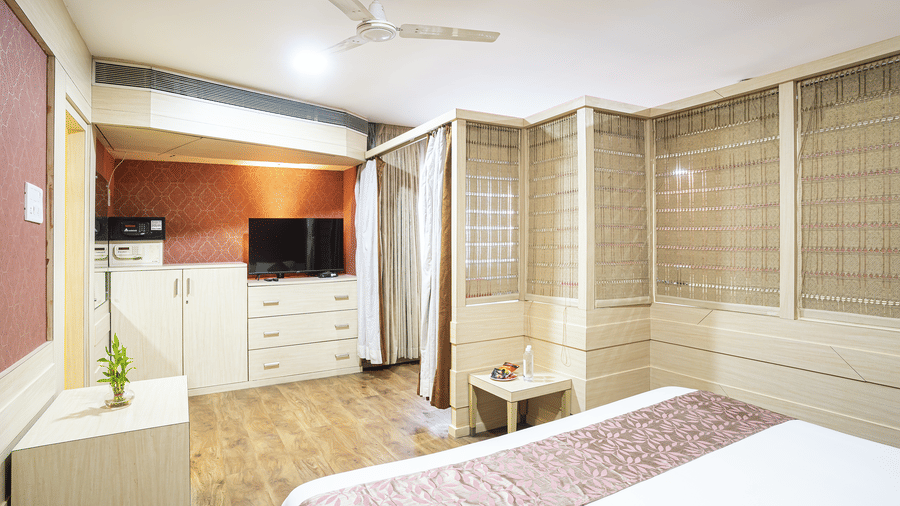 A room with a king size bed, wooden flooring, television and white wardrobe at Infiniti Hotel, Indore.