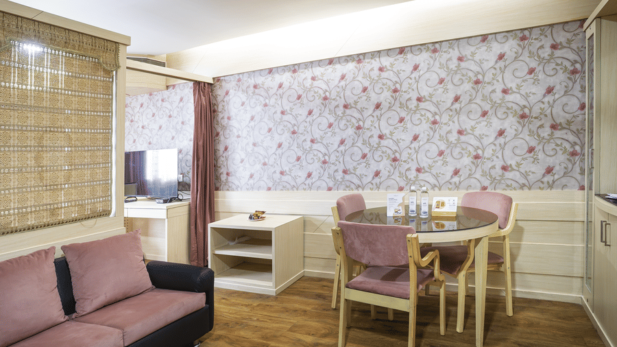 A suite with sofa, dining table, floral wallpaper and wooden flooring at Infiniti Hotel, Indore.