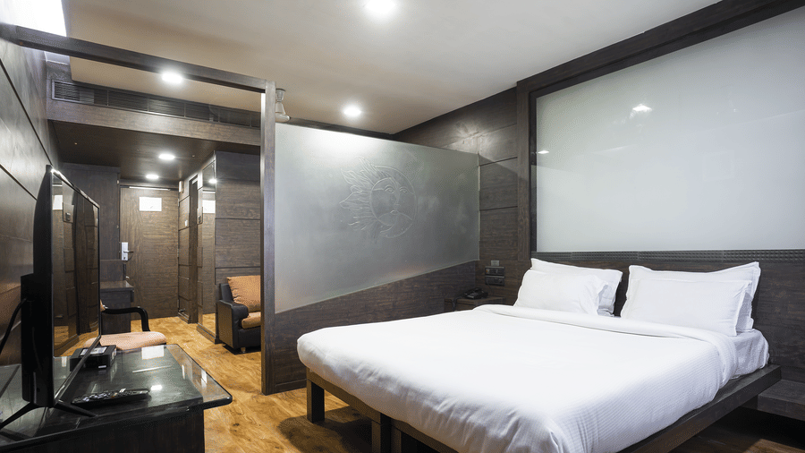 Bedroom with a king size bed, side table and dark wall panels at Infiniti Hotel, Indore.