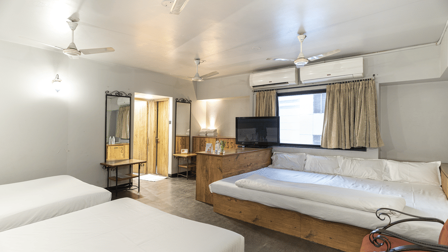 A spacious room with 3 beds, wooden furniture and curtains at Infiniti Hotel, Indore.