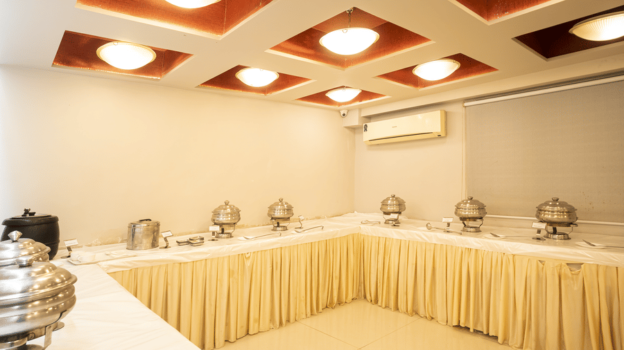 A banquet hall with tables covered in cream cloth, buffet counters and modern ceiling lights at Infinit Hotel, Indore.