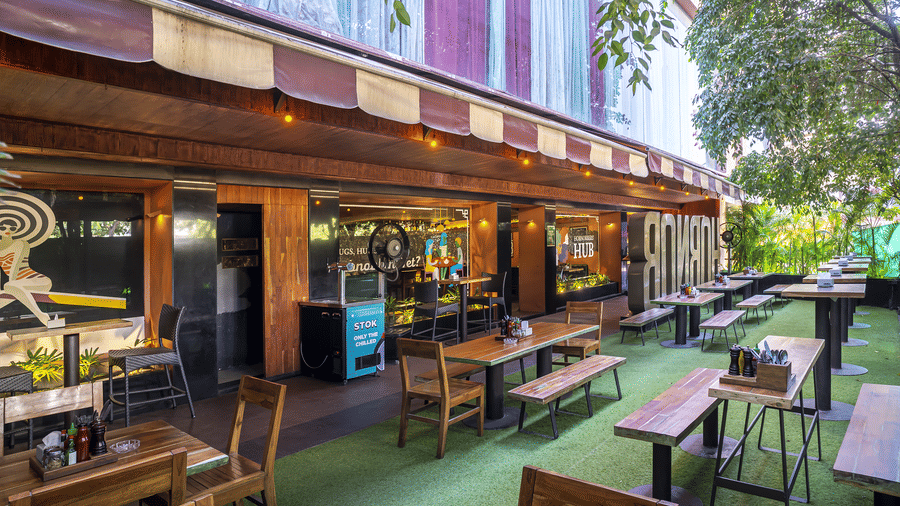 An outdoor seating area with tables, chairs and a long building wall decorated with signs at Infiniti Hotel, Indore.