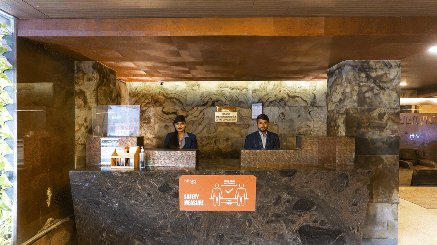 Reception area with a large marble counter, hotel staff standing behind it, and warm wooden ceiling panels at Infiniti Hotel, Indore.