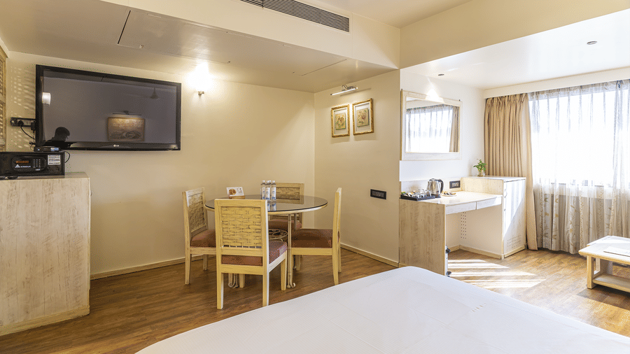 A room with king size bed, television, dining table and wooden flooring at Infiniti Hotel, Indore.