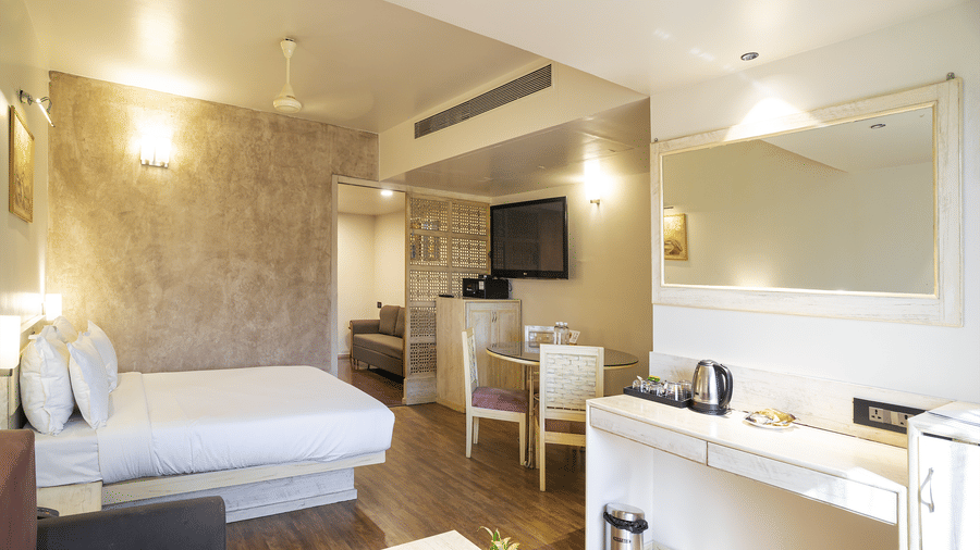 A suite with king size bed, dining table & chairs, television and wooden furniture at Infiniti Hotel, Indore.