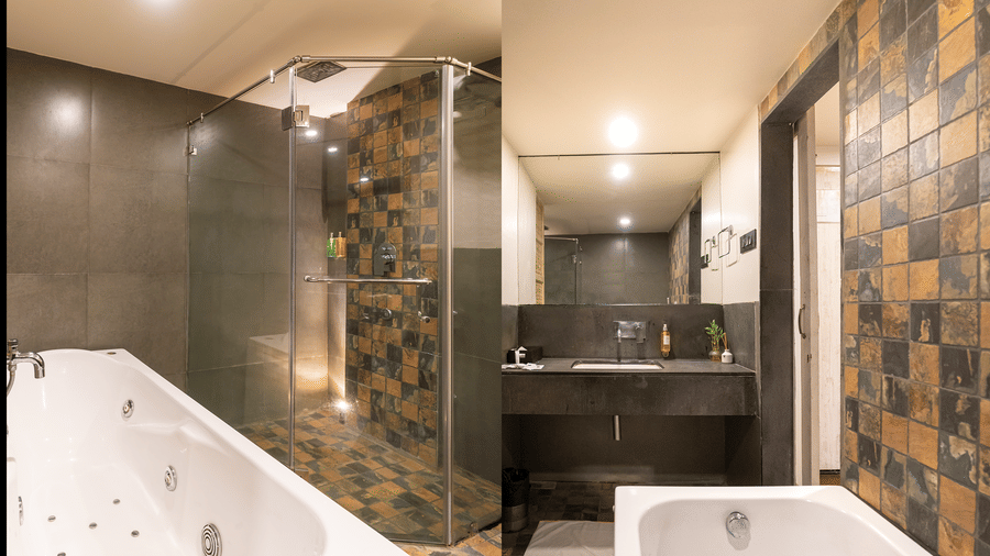 A bathroom with a bathtub, patterned tiled walls and washbasin at Infiniti Hotel, Indore.