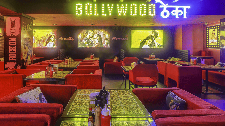 A restaurant interior with red sofas, patterned tables and a glowing signboard reading 'BOLLYWOOD ????' at Infiniti Hotel, Indore.