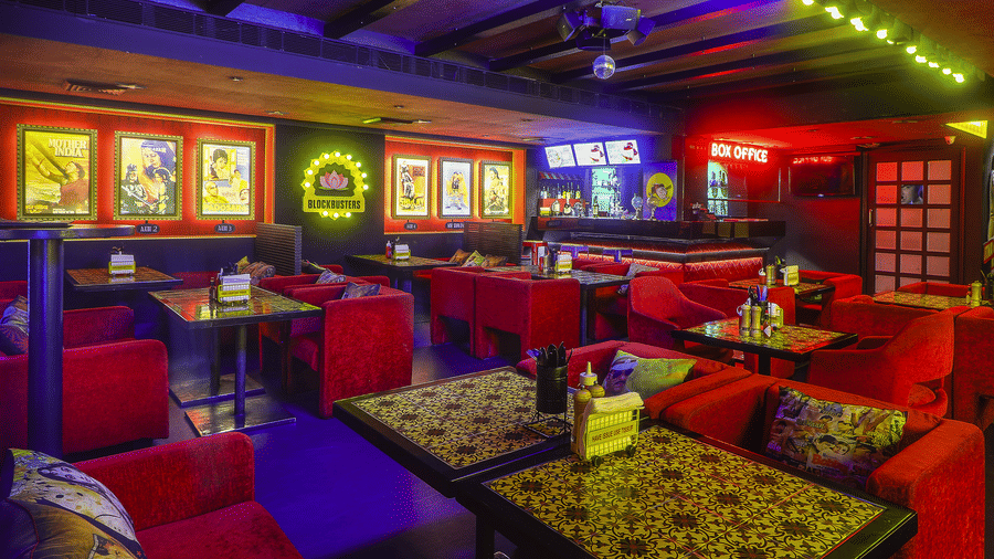Rows of red sofas and dining tables with framed Bollywood posters and neon lights at Infiniti Hotel, Indore.