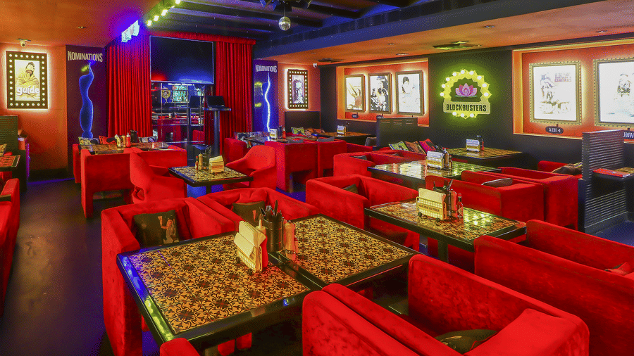 A restaurant hall with multiple red sofas, framed posters and bright neon lights at Infiniti Hotel, Indore.