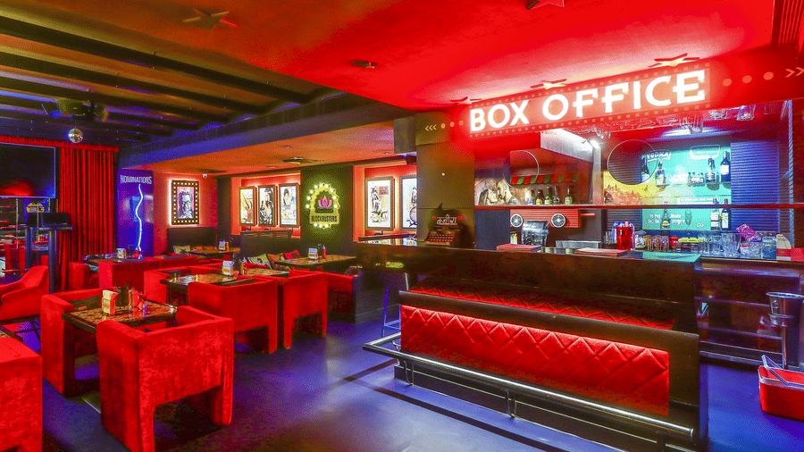 A bar counter with a glowing 'BOX OFFICE' sign and red sofas in front at Infiniti Hotel, Indore.