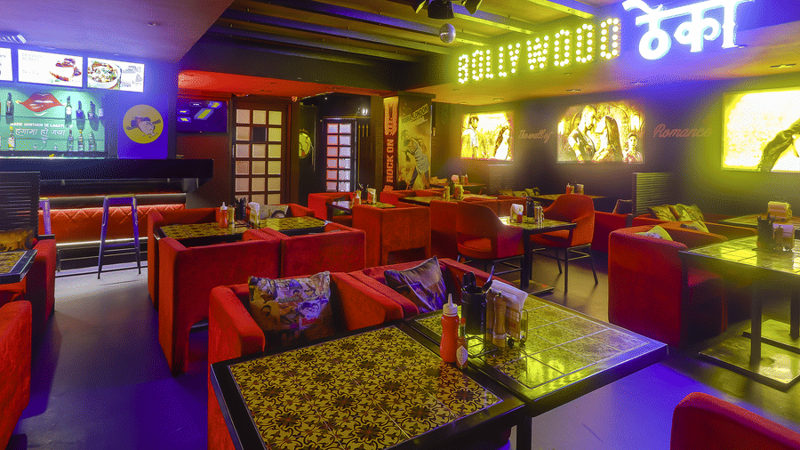 Dining tables with red sofas, decorative wall posters and a yellow neon sign at Infiniti Hotel, Indore.
