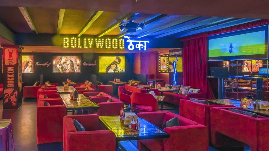 A restaurant interior with red sofas, wall posters and a glowing signboard reading 'BOLLYWOOD ????' at Infiniti Hotel, Indore.