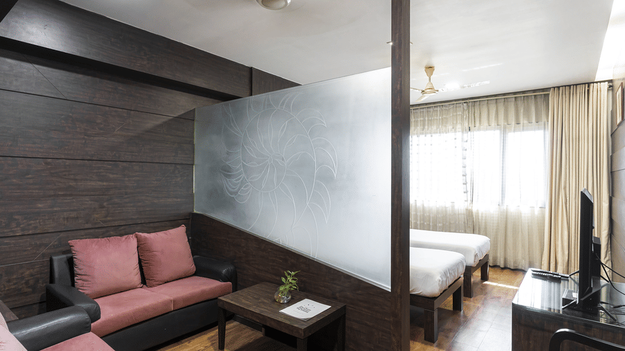 A bedroom at Infiniti Hotel, Indore featuring 2 sofas, coffee table, frosted glass partition, single beds, and television.