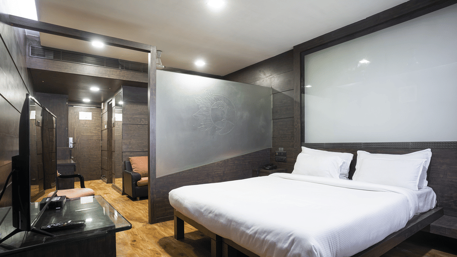A bedroom at Infiniti Hotel, Indore featuring king size bed, television console, frosted glass divider, and entrance hallway.