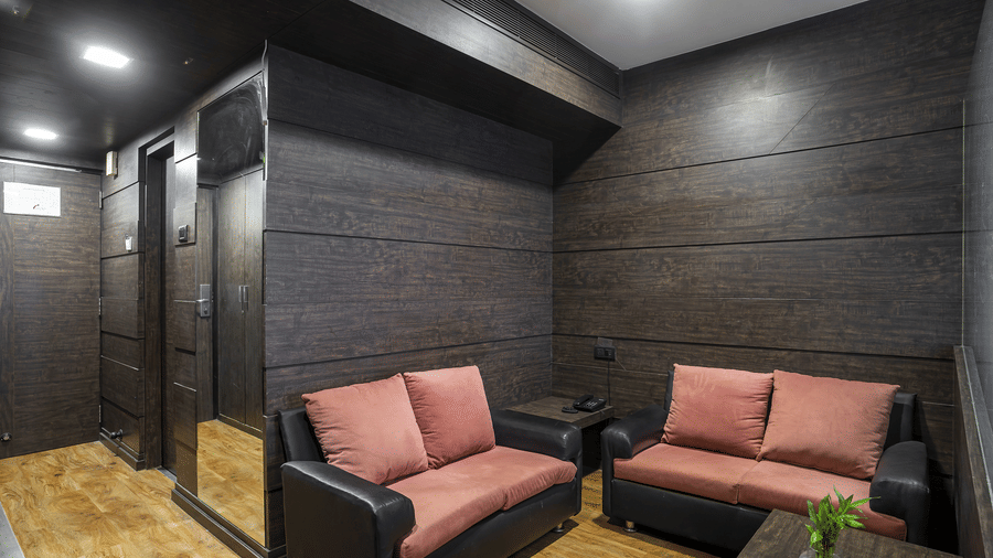A seating area at Infiniti Hotel, Indore featuring 2 sofas, side table, desk lamp, and wooden paneled walls.