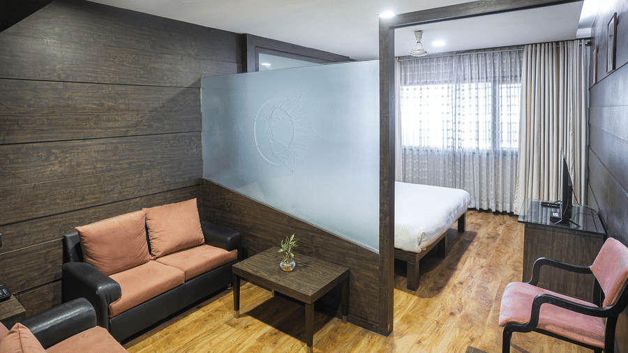 A bedroom at Infiniti Hotel, Indore featuring 2 sofas, coffee table, frosted glass screen, double bed, and chair.