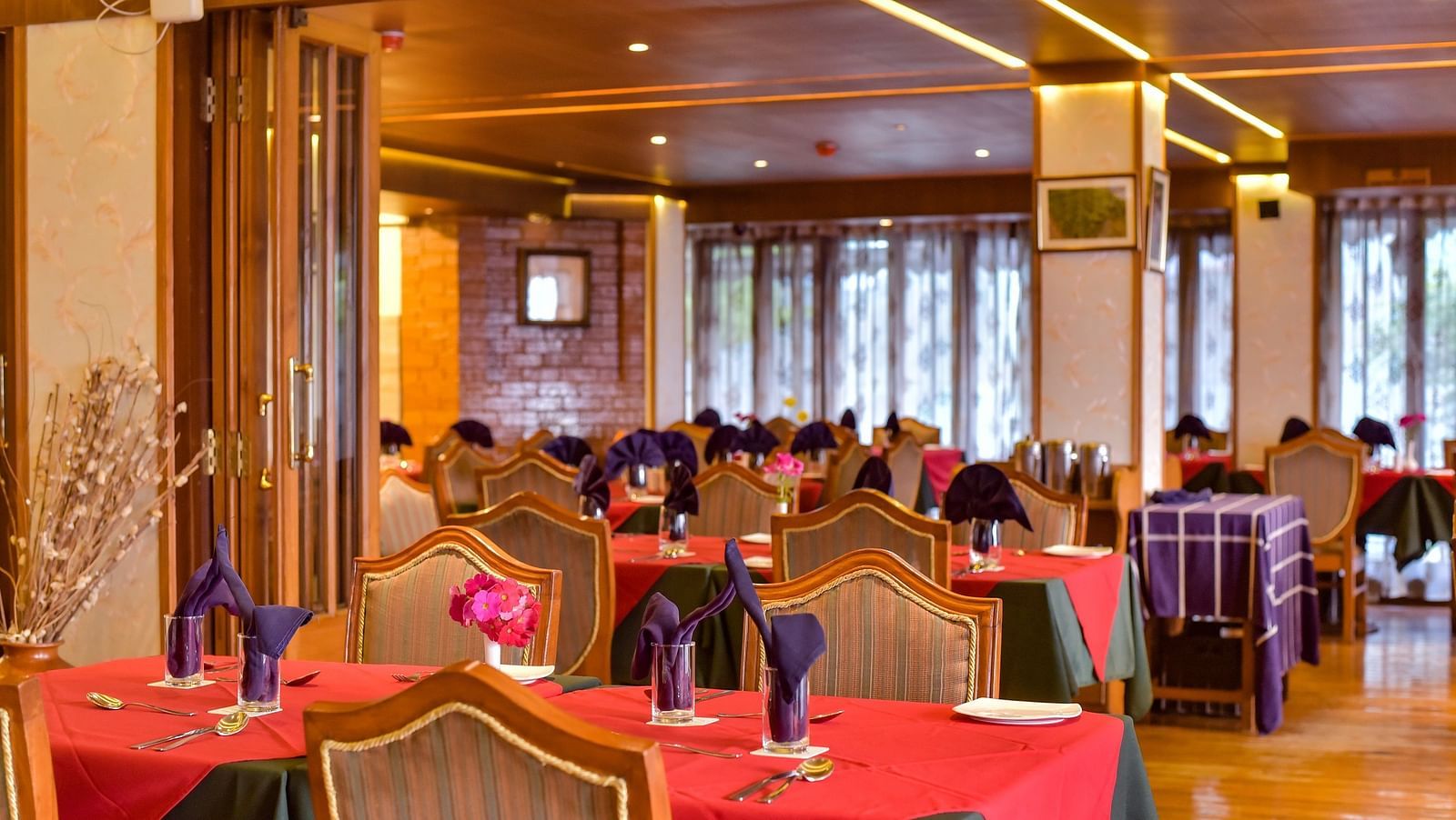 Dining area at Cedar Inn, Darjeeling, featuring elegant wooden interiors, red and green tablecloths, and neatly folded napkins on each table.