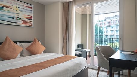 A bedroom with a bed, pillows, a nightstand, a table, a chair, and a window with a view | Three-bedroom Suite | Central Mansions, Phnom Penh