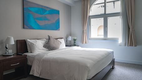 A bedroom with a large bed, a nightstand, and a painting on the wall | Two-bedroom Suite | Central Mansions, Phnom Penh
