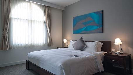 A well-lit bedroom with a large bed, a nightstand, and a modern painting above the headboard | One-bedroom Suite | Central Mansions, Phnom Penh