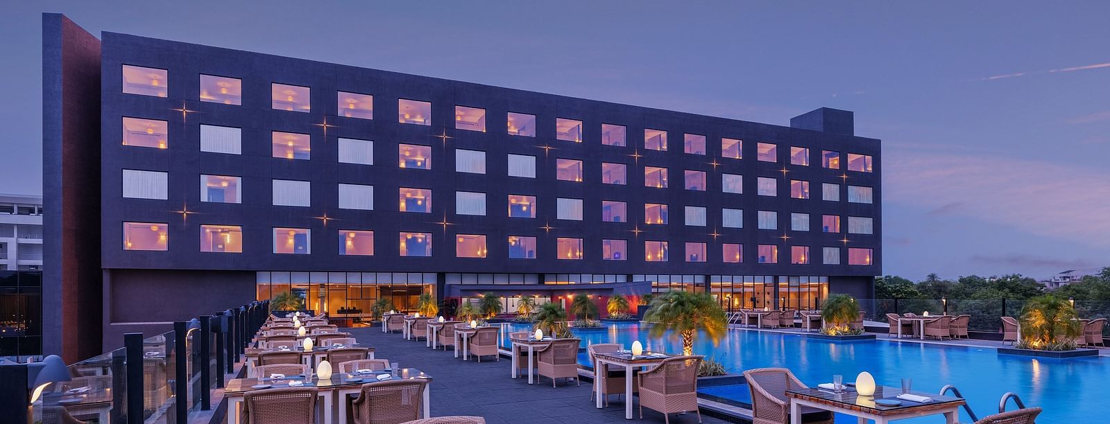 Facade of Essentia Luxury Hotel, Indore with a pool in front and dining space besides the table at Essentia Luxury Hotel, Indore